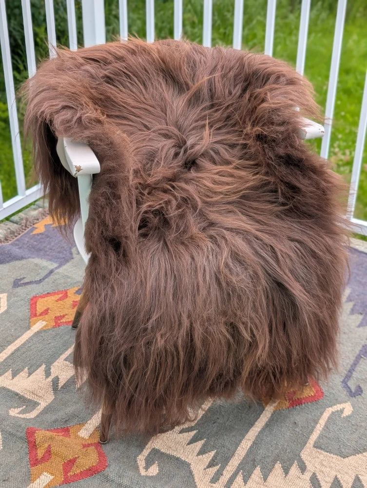 A thick fluffy brown icelandic sheepskin rug with long wool draped over a white chair by angus oliver