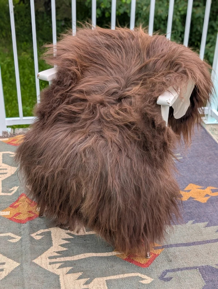 A thick fluffy brown long wool icelandic sheepskin rug draped over a white chair by angus oliver