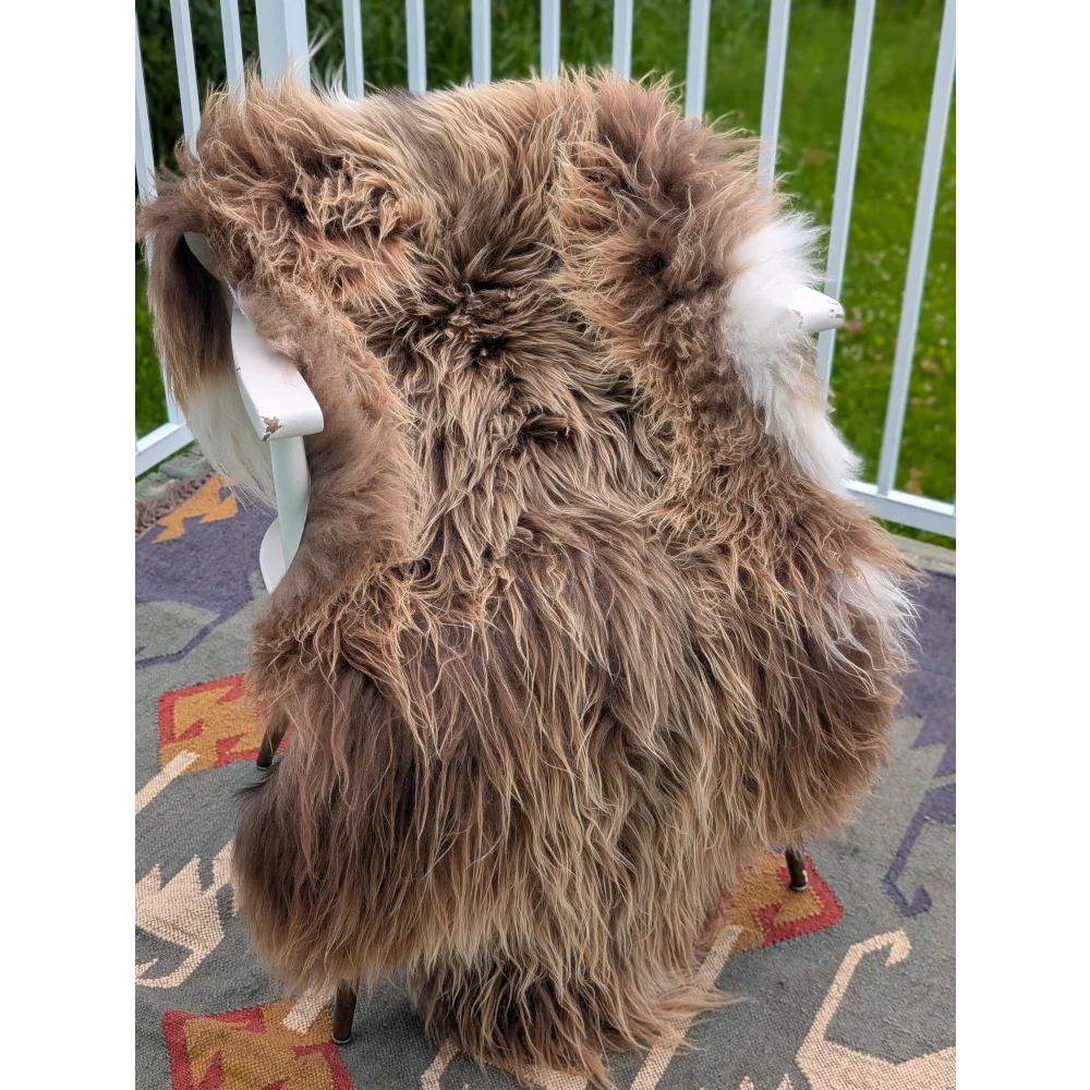 A thick fluffy brown icelandic sheepskin rug with long wool and subtle white accents draped over a chair back