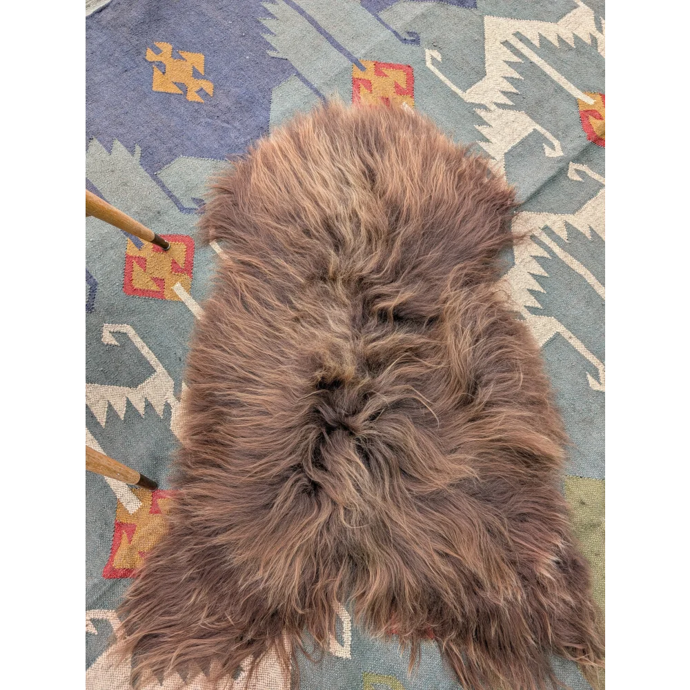 A plush brown long wool icelandic sheepskin rug with dense fur by angus oliver lying flat on a patterned carpet