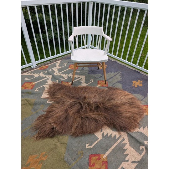 A fluffy brown long wool icelandic sheepskin rug with natural shaggy texture on an intricate carpet by angus oliver