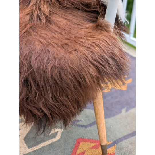 A plush long wool icelandic sheepskin in brown draped over a wooden chair back in extra large size 48 x 35 inches