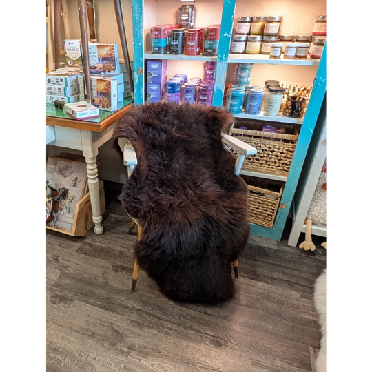 A plush extra large dark brown british sheepskin rug draped over a white wooden chair by angus oliver