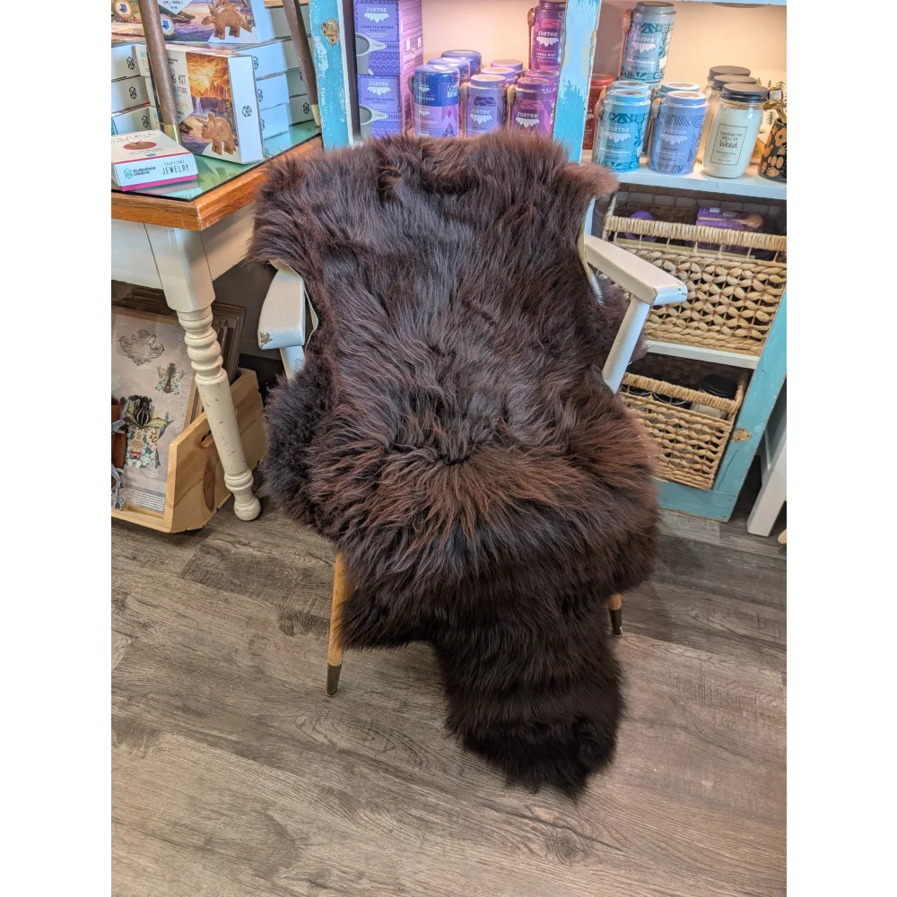 A plush extra large dark brown british sheepskin rug draped over a white wooden chair by angus oliver