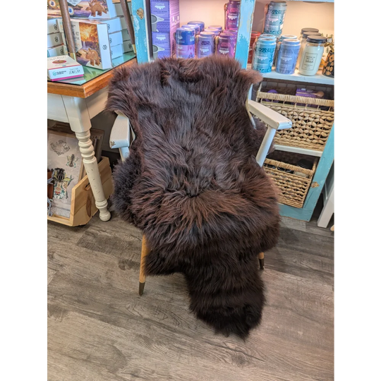 A plush extra large dark brown british sheepskin rug draped over a white wooden chair by angus oliver