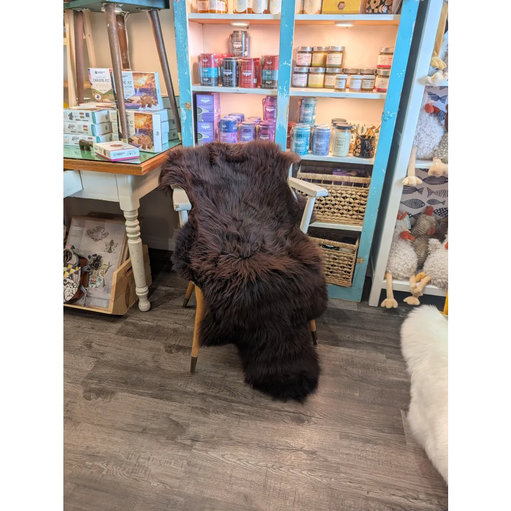 A dark brown extra large british sheepskin rug draped over a wooden chair from angus oliver standard grade