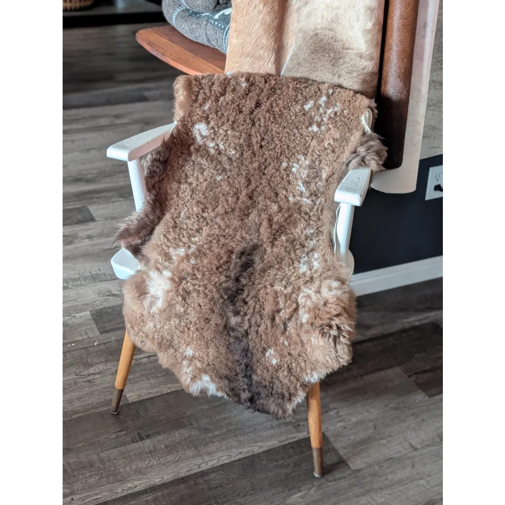 Brown fluffy tibet highland spotted sheepskin rug draped over white wooden chair showcasing soft texture