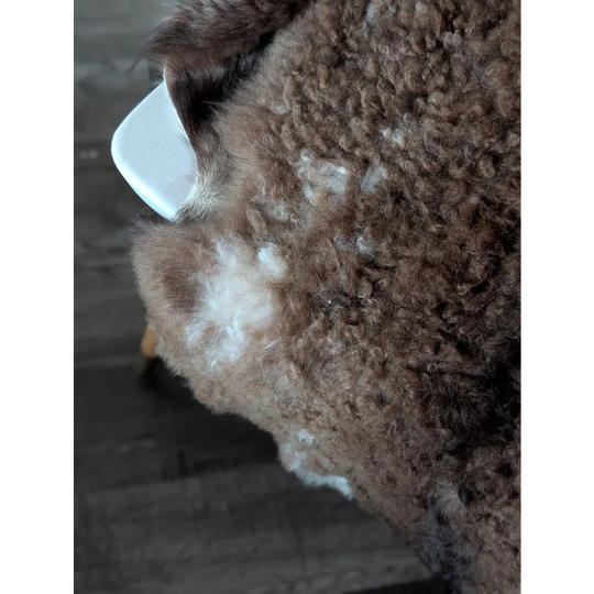 A fluffy brown dog with curly fur and a white patch on its back laying on a tibet highland spotted sheepskin rug
