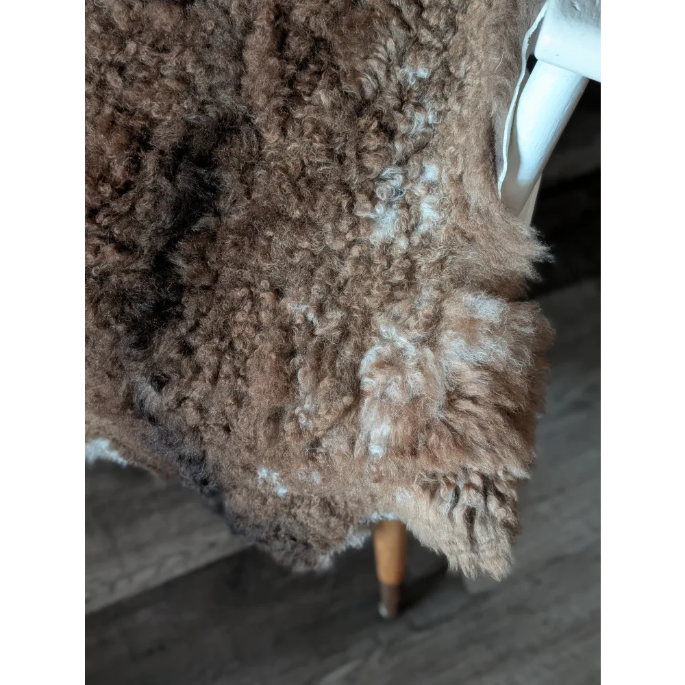 Cozy brown tibet highland spotted sheepskin rug draped over chair leg showing soft curly texture