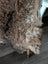 Cozy brown tibet highland spotted sheepskin rug draped over chair leg showing soft curly texture