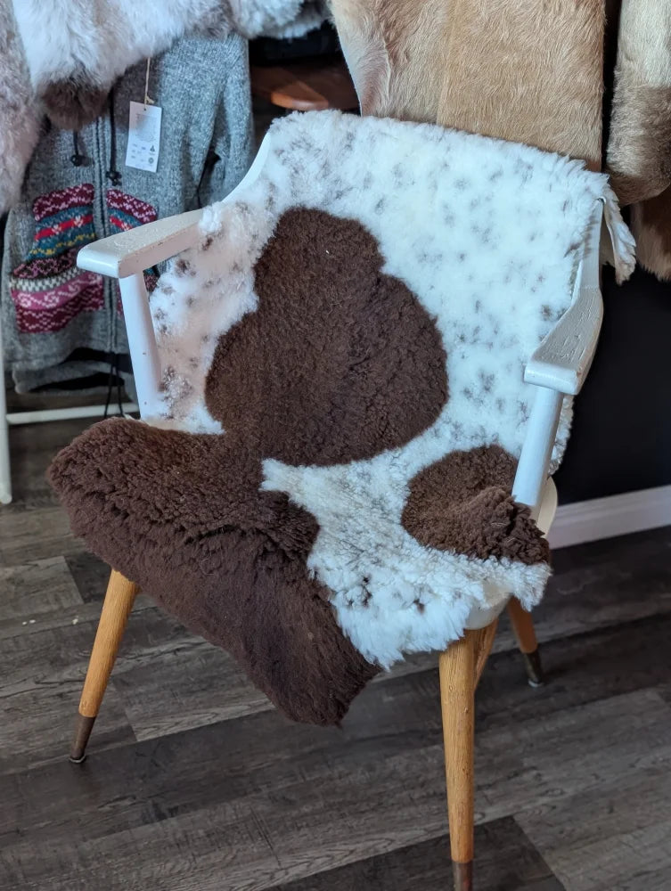 Cozy white and brown tibet highland spotted grade a- sheepskin chair cover draped over wooden armchair frame