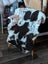A plush black and white cow print grade a sheepskin rug from tibet highland spotted draped over a white wooden chair