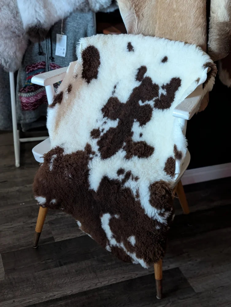 A plush brown and white tibet highland spotted grade a- sheepskin rug draped over a wooden chair from nat’s grade