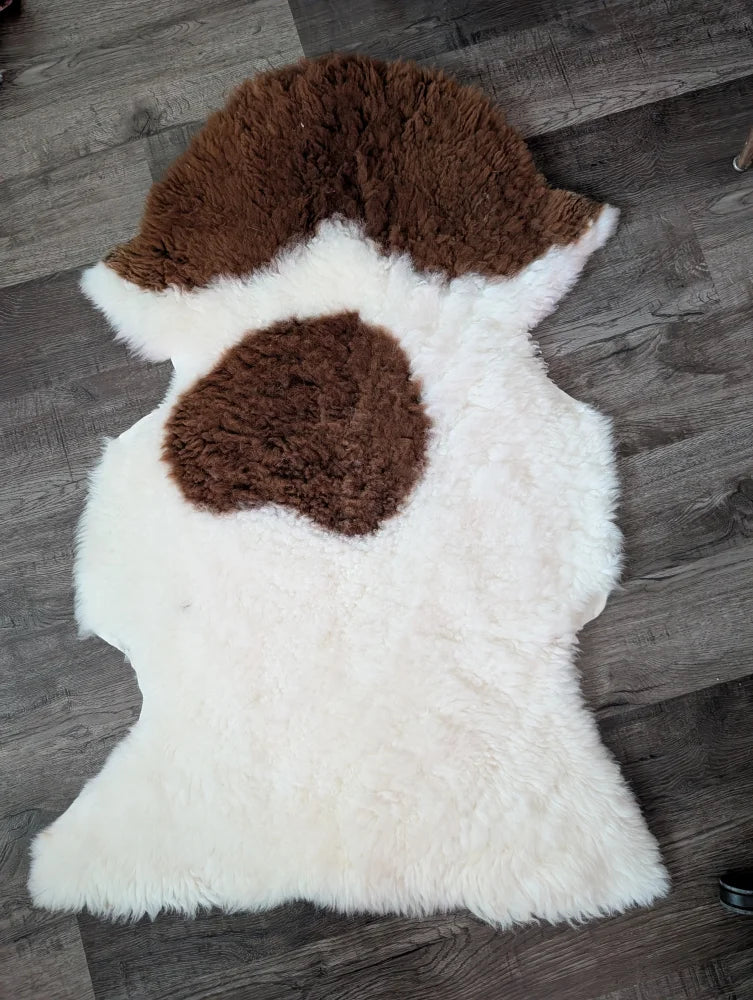 A plush white and brown tibet highland spotted grade a- sheepskin rug with a fluffy natural texture from nat’s grade