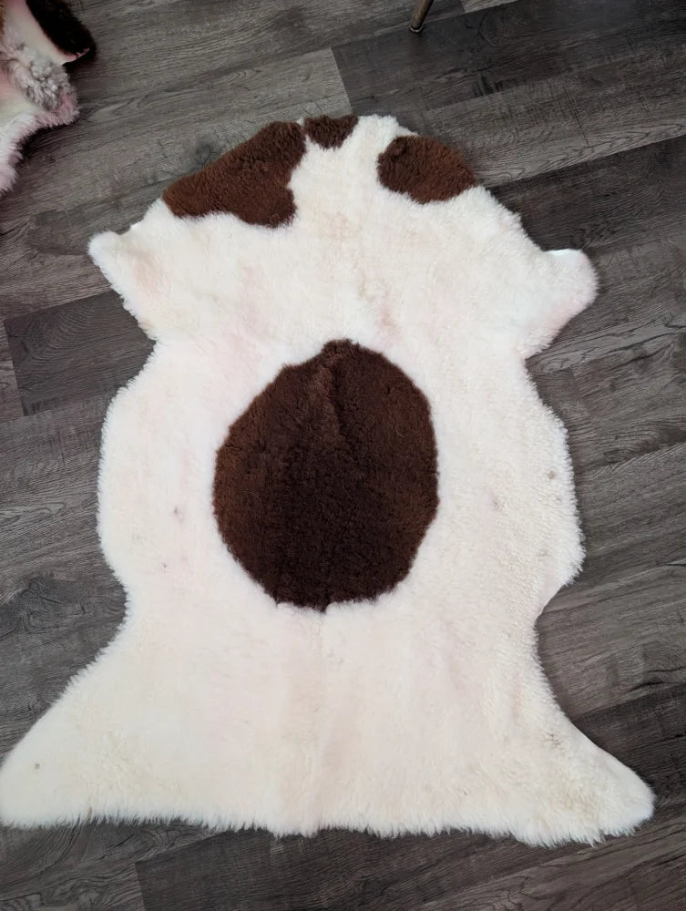 A plush white and brown grade a- sheepskin tibet highland spotted rug with fluffy texture and dark brown patches
