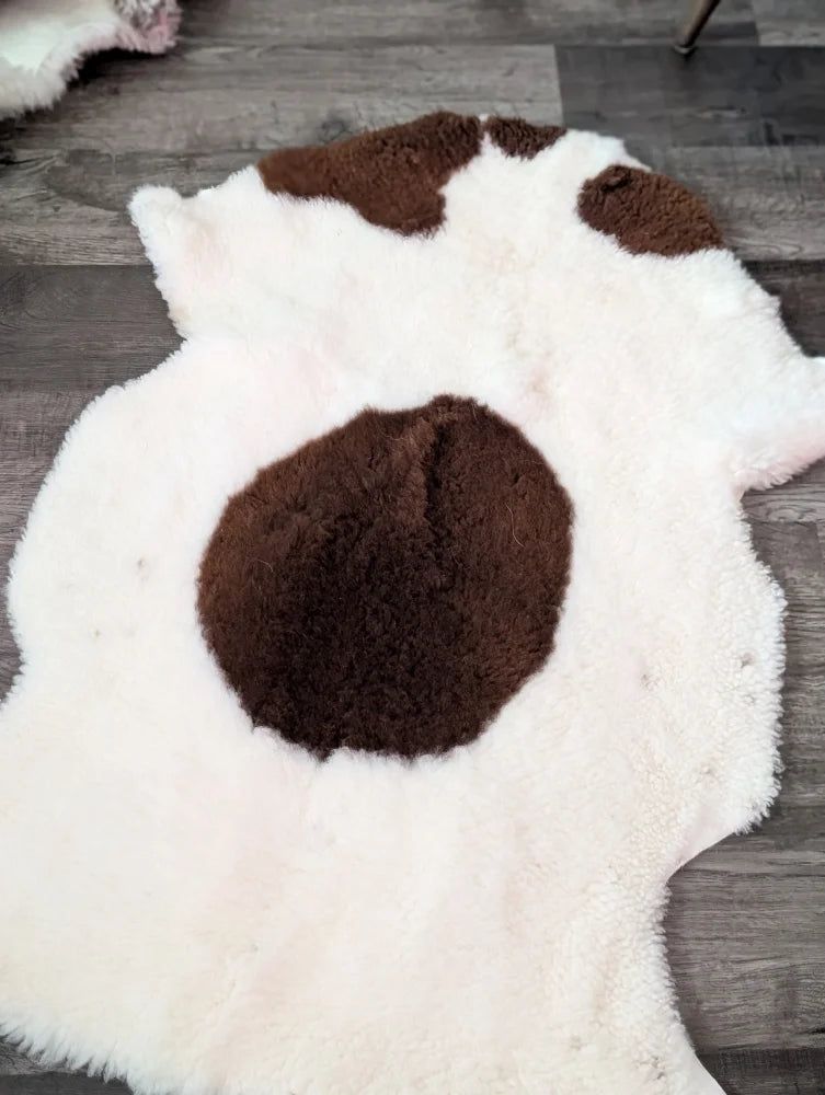 A plush white and brown tibet highland spotted grade a- sheepskin rug with natural fluffy texture from nat’s grade