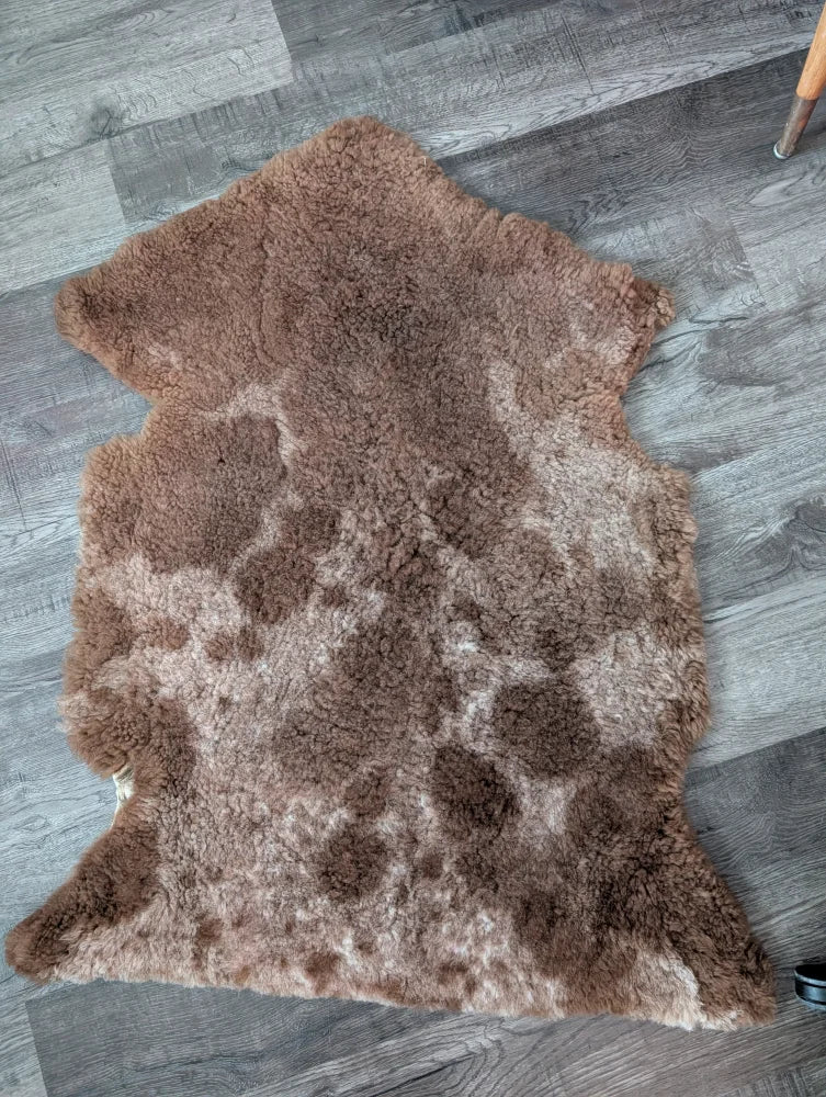A soft natural brown tibet highland spotted grade a- sheepskin rug with plush tan patches and fluffy texture
