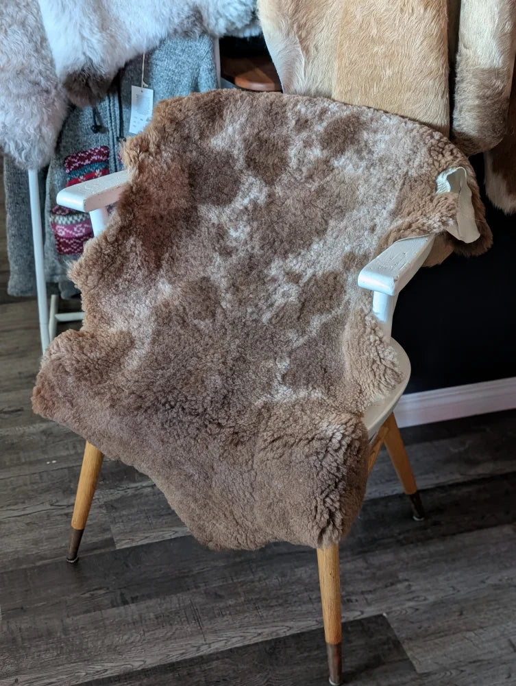 A soft natural brown tibet highland spotted grade a- sheepskin rug with fluffy texture draped over a white wooden chair