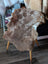 A soft natural brown tibet highland spotted grade a- sheepskin rug with fluffy texture draped over a white wooden chair