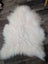 A large natural white icelandic sheepskin rug with long soft wool lying on a dark wooden floor from curated collection