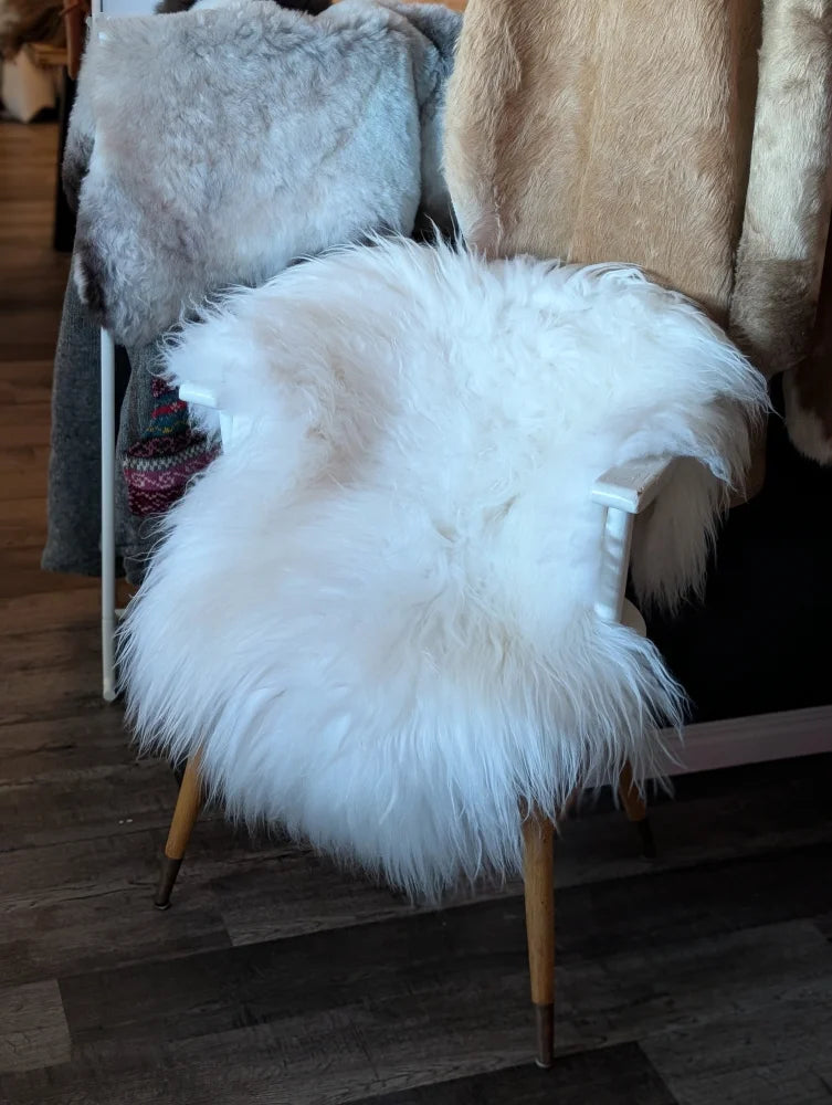A large natural white icelandic sheepskin rug draped over a chair with wooden legs from a curated collection of wool icelandic sheepskins