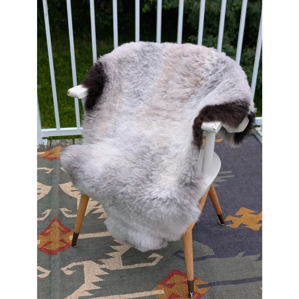 A plush gray and black long wool icelandic sheepskin rug draped over a white chair with wooden legs by angus oliver