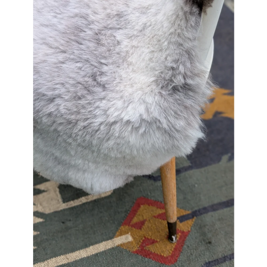 A plush light gray long wool icelandic sheepskin chair cover draped over the back of a modern wooden chair by angus oliver