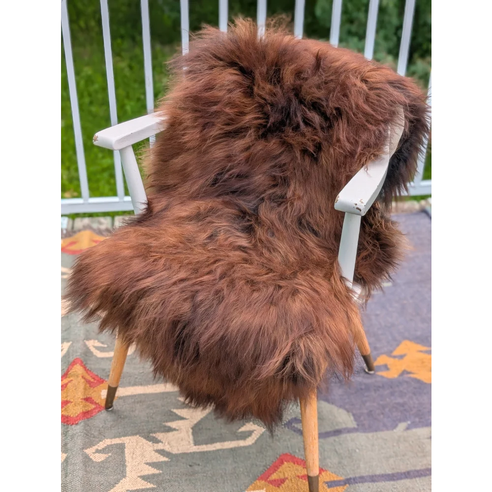 A plush rich brown long wool icelandic sheepskin rug draped over a white wooden chair with light wood legs