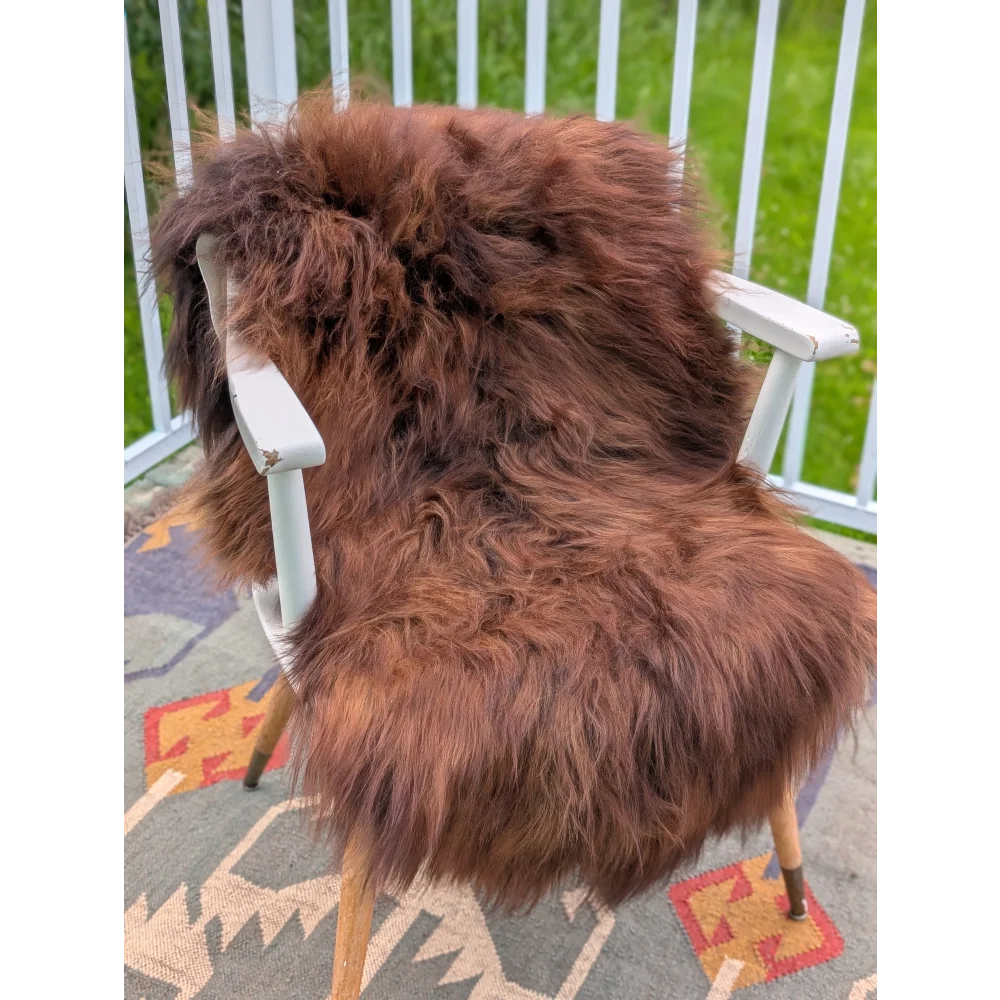 A plush rich brown icelandic sheepskin throw with long wool draped over a white wooden chair for cozy comfort