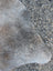 A large grayish-brown lovely cowhide rug with unique characteristics lying on a speckled concrete ground