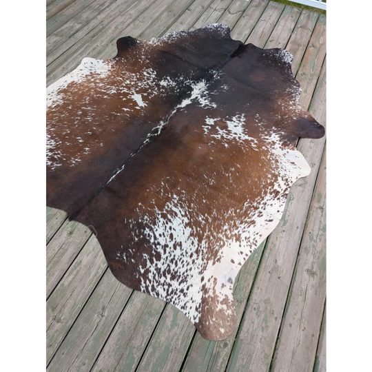 Brown and white spotted large cowhide rug with unique characteristics laid out on wooden deck for stylish decor