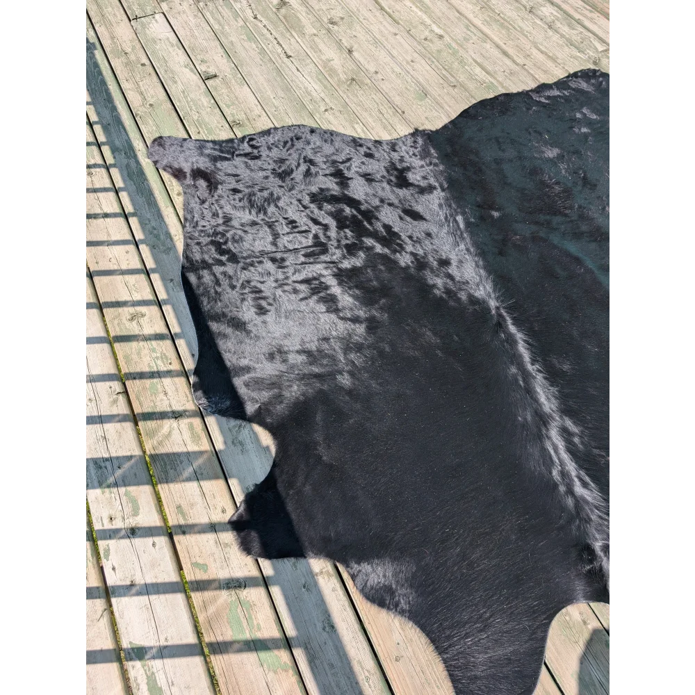 A large angus oliver black cowhide rug with mottled black and gray pattern lies flat on weathered wooden planks