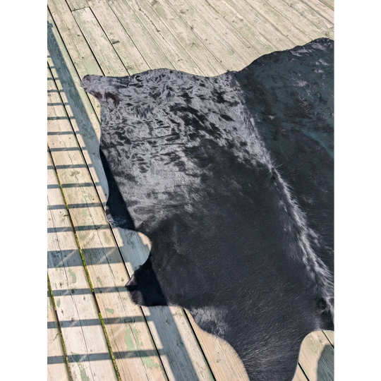A large angus oliver black cowhide rug with mottled black and gray pattern lies flat on weathered wooden planks