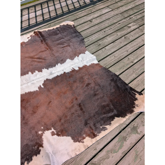 Large brown and white angus oliver cowhide rug with natural fur texture laid on wooden deck perfect for decor