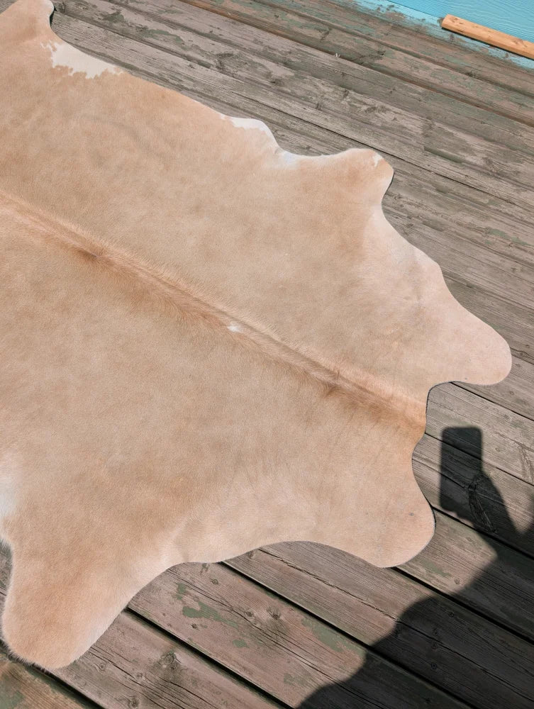 Beige large cowhide rug with natural fur texture and irregular edges laid flat on weathered wooden deck angus oliver
