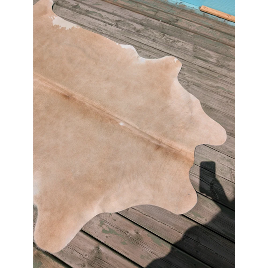 Beige large cowhide rug with natural fur texture and irregular edges laid flat on weathered wooden deck angus oliver