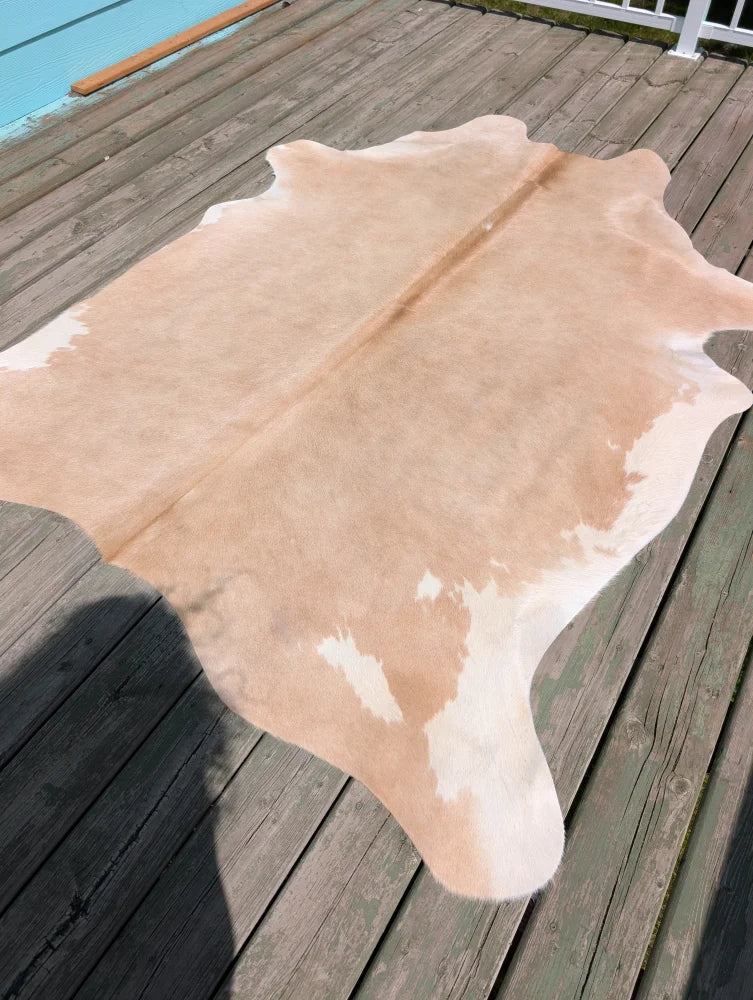 T#18 77 x 63 gorgeous large cowhide rug in natural tan and white by angus oliver on a wooden deck
