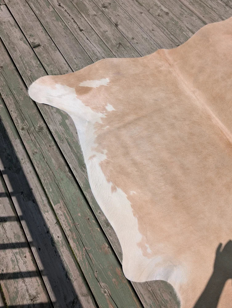 A large tan and white cowhide rug with natural edges lying flat on a weathered deck by angus oliver