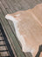A large tan and white cowhide rug with natural edges lying flat on a weathered deck by angus oliver