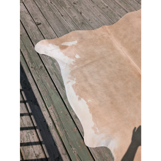 A large tan and white cowhide rug with natural edges lying flat on a weathered deck by angus oliver