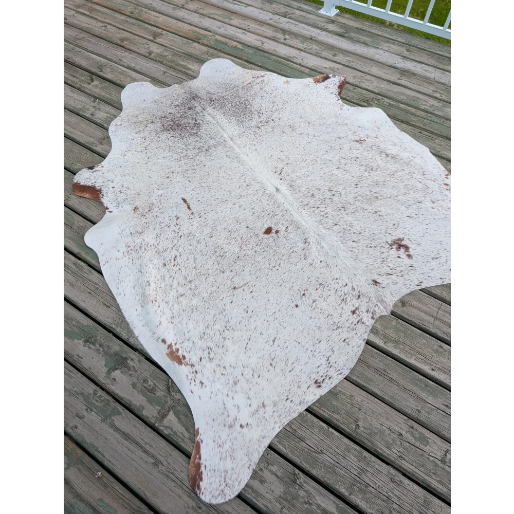 Large cowhide rug with white and brown speckled pattern and natural irregular edges showcasing unique characteristics