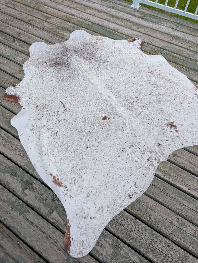 Large cowhide rug with white and brown speckled pattern and natural irregular edges showcasing unique characteristics