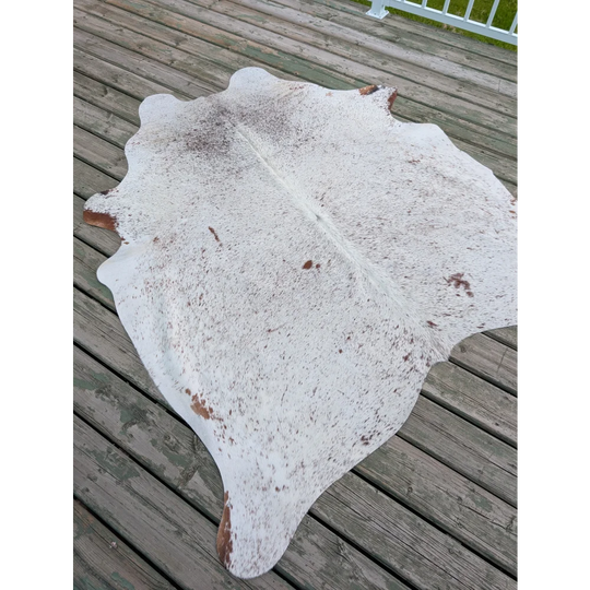 Large cowhide rug with white and brown speckled pattern and natural irregular edges showcasing unique characteristics