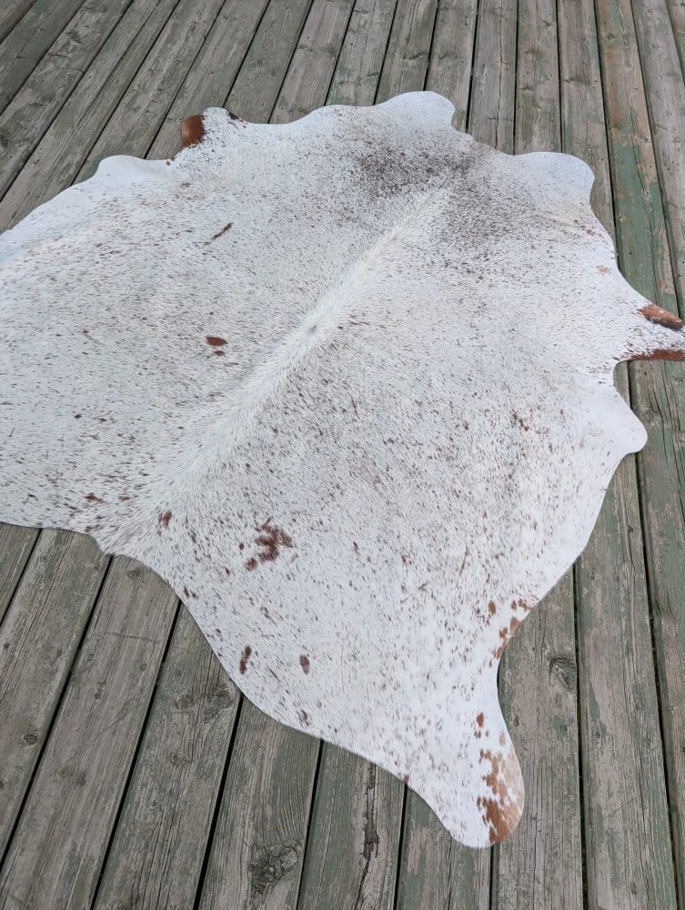 T#2 heart 73 x 63 gorgeous large cowhide rug with brown speckles and natural edges on a wooden deck showing unique characteristics