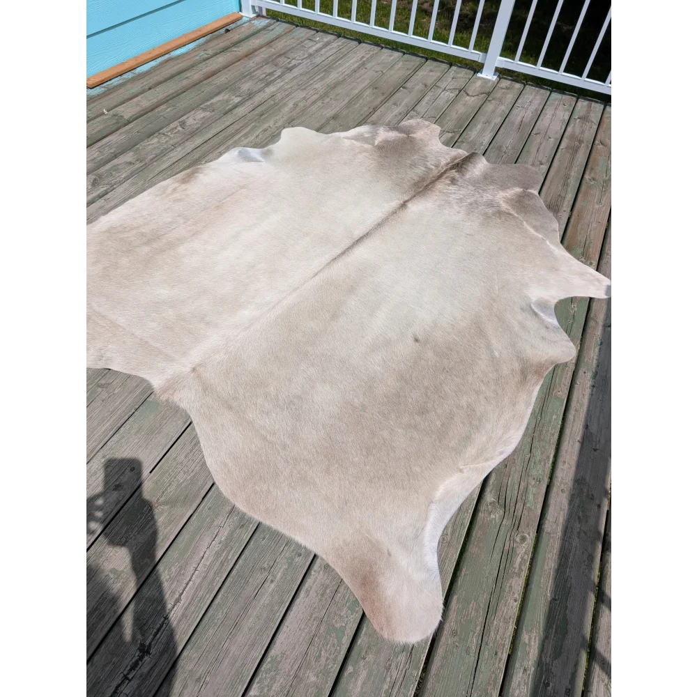 Large cowhide angus oliver rug in light beige with soft texture and irregular edges on wooden deck