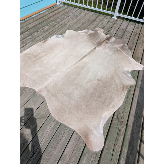 Large cowhide angus oliver rug in light beige with soft texture and irregular edges on wooden deck