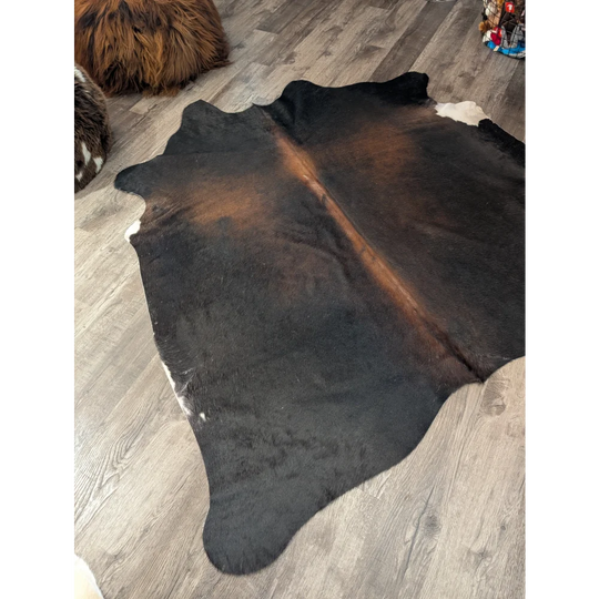 Large cowhide angus oliver rug in natural black brown with white patches laid flat on wooden floor