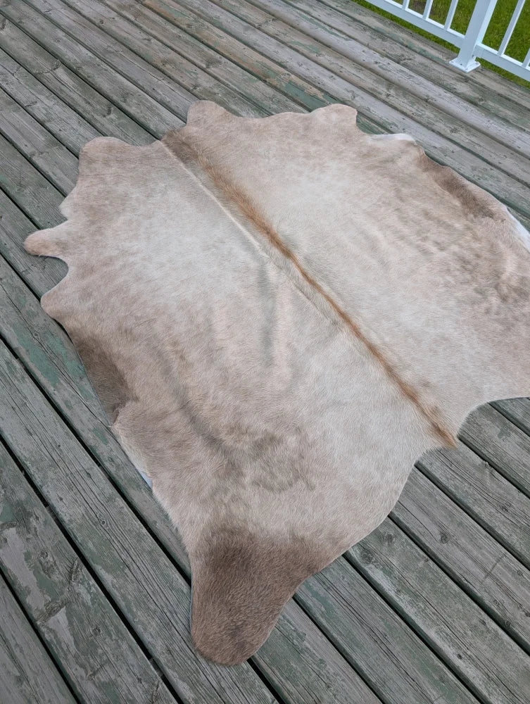 A natural-toned, full-sized cowhide rug with a soft, textured surface and subtle brownish patches.