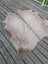 A natural-toned, full-sized cowhide rug with a soft, textured surface and subtle brownish patches.