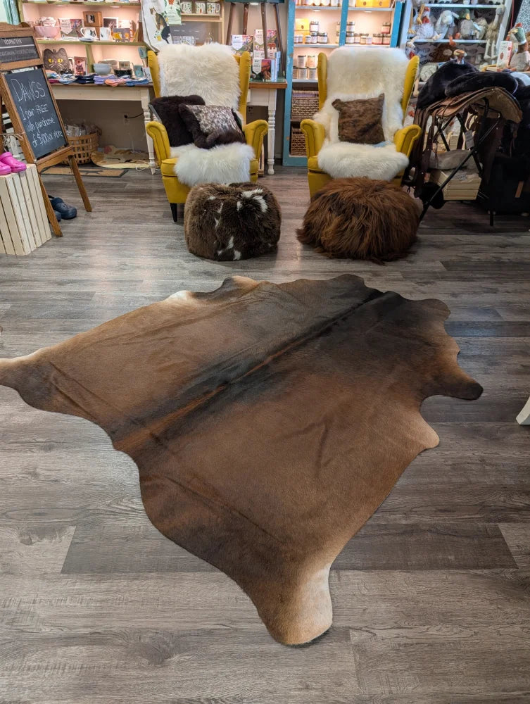 Large brown angus oliver cowhide rug with natural irregular edges and soft textured surface measuring 77 x 66 inches